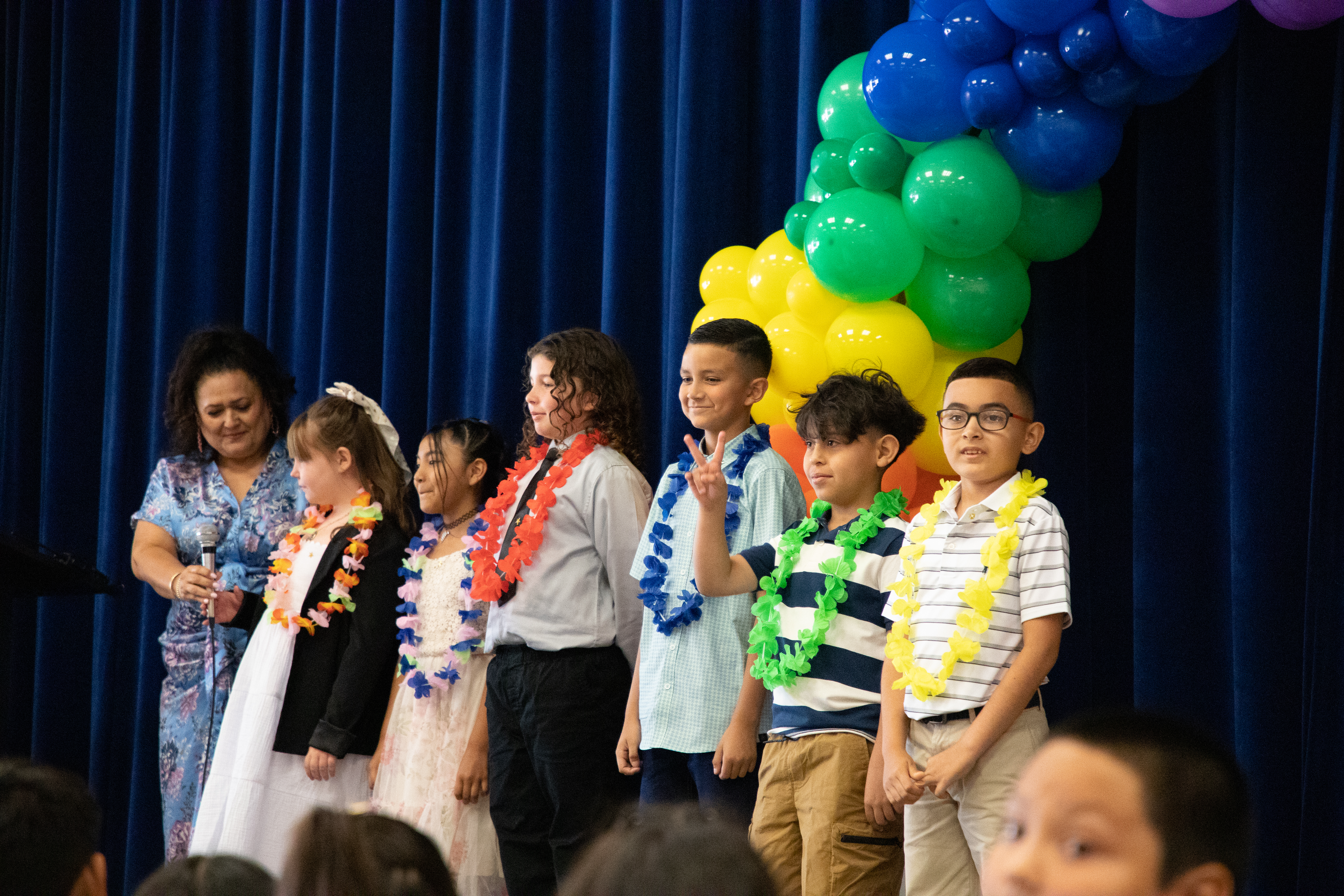 A group of students on stage with a rainbow balloon arch