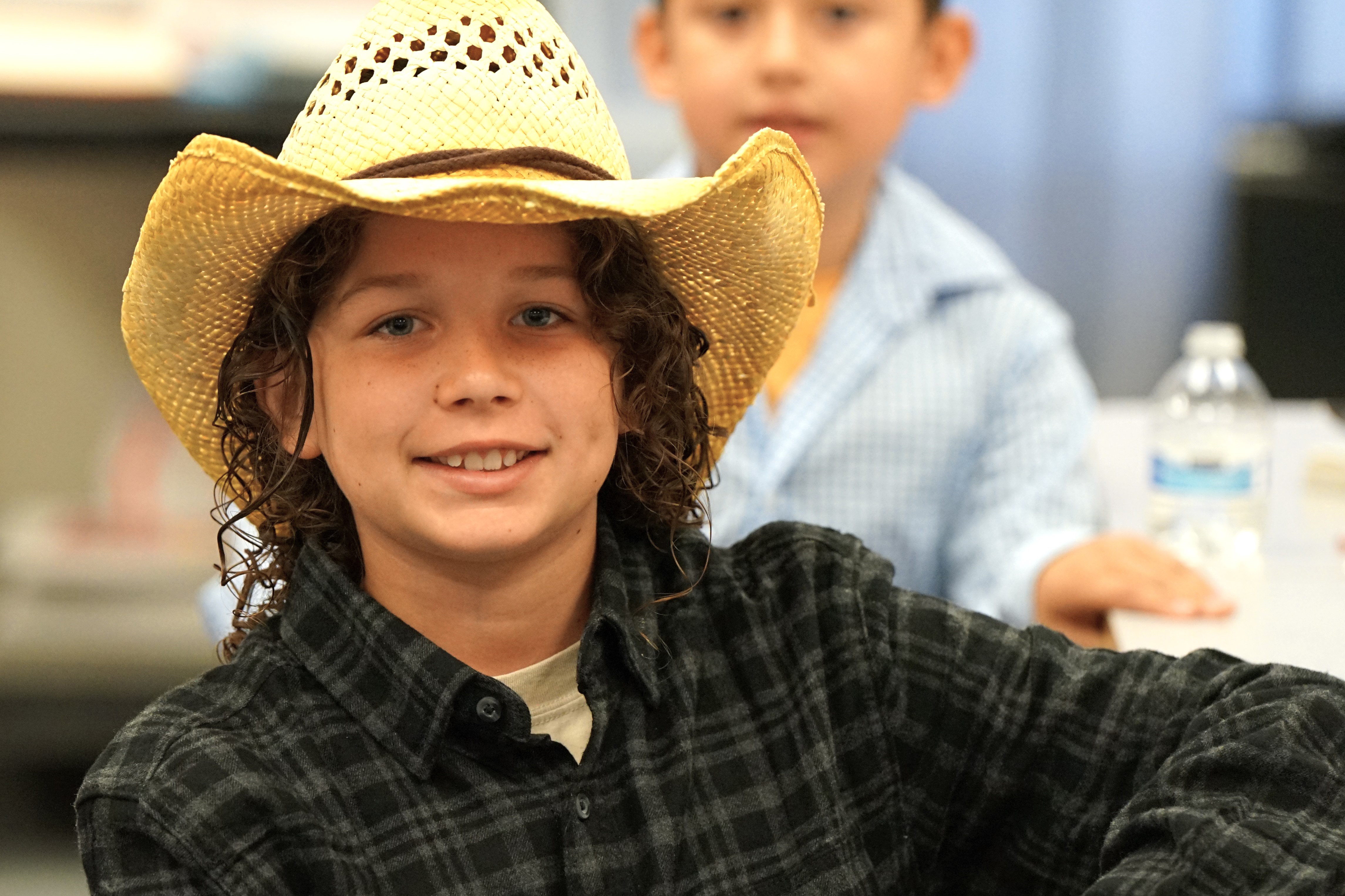 A boy in a cowboy hat and plaid shirt smiles