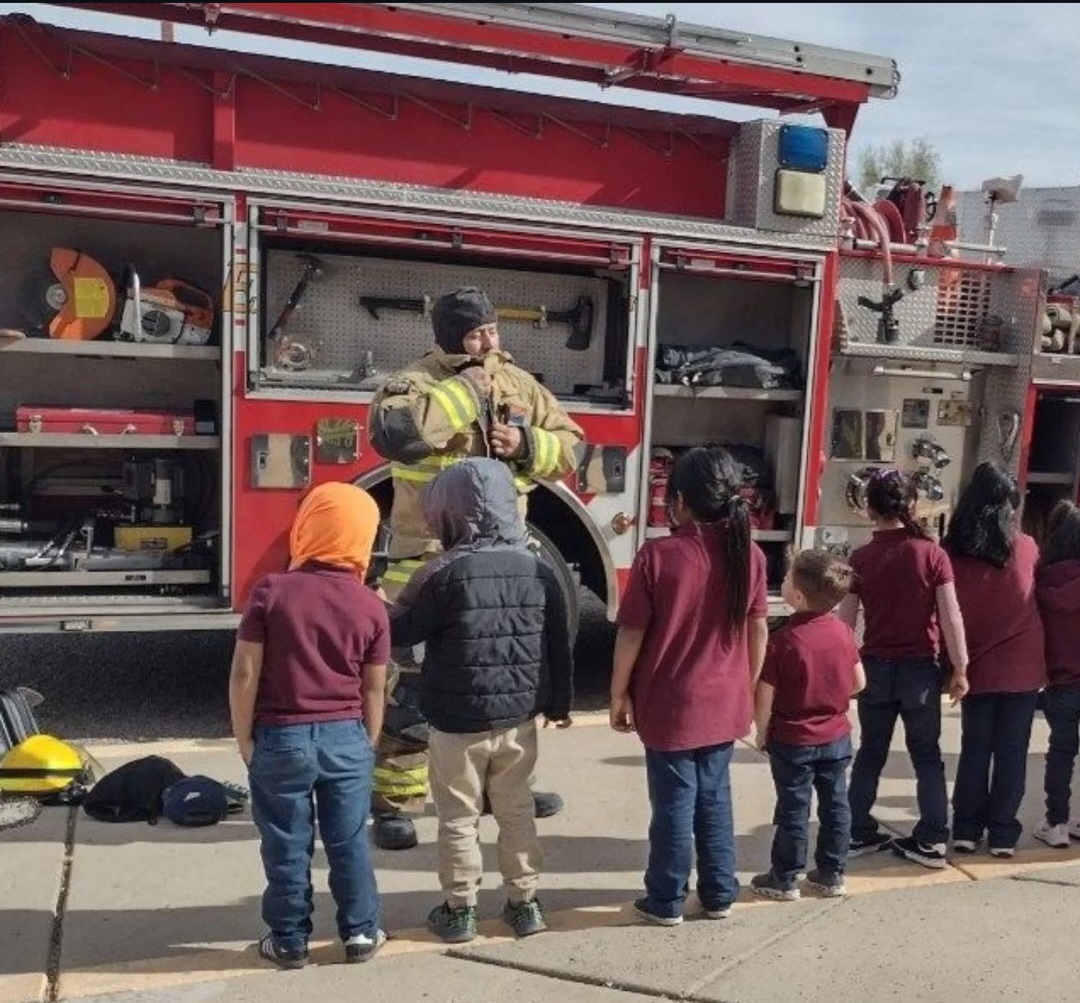 A firefighter shows off safety equipment on his truck to kindergarten students