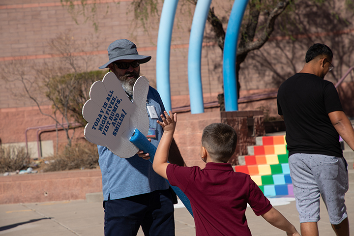 A man holds up a giant hand cutout on a pool noodle as a boy comes by to give it a high five