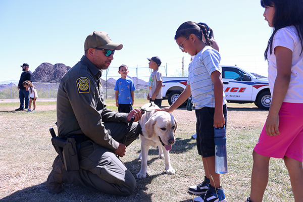 A man holds a yellow lab on a leash as students pet the dog