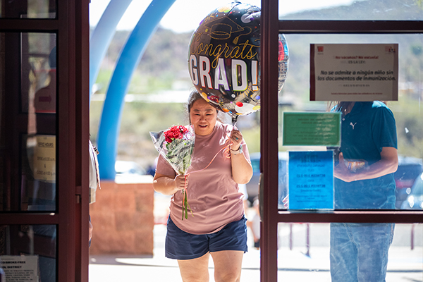 A woman walks into the school with a grad balloon