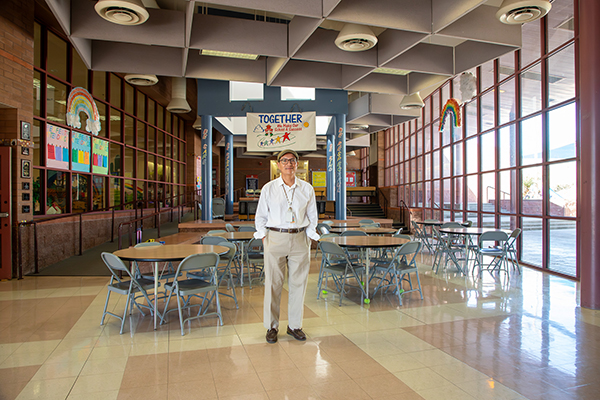 A man in a white dress shirt and khakis stands in the cafeteria
