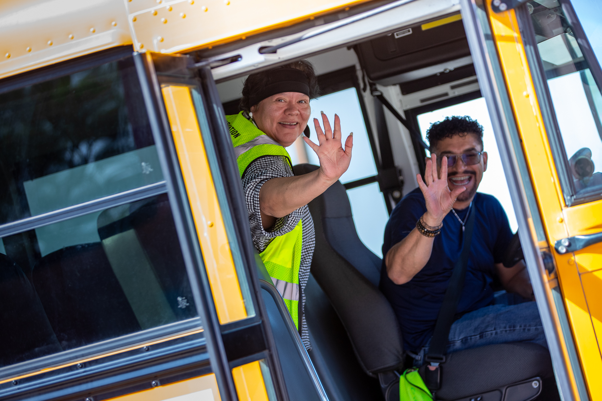 A bus driver and School Safety monitor wave from the school bus