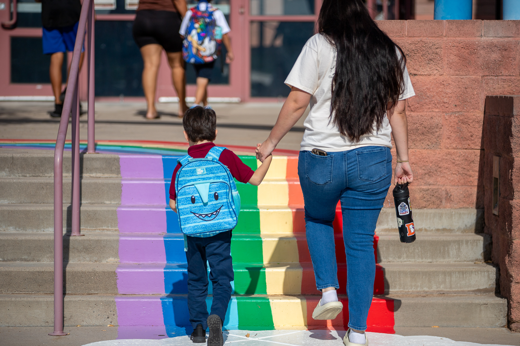 A boy and his mom walk up the rainbow-painted steps into school