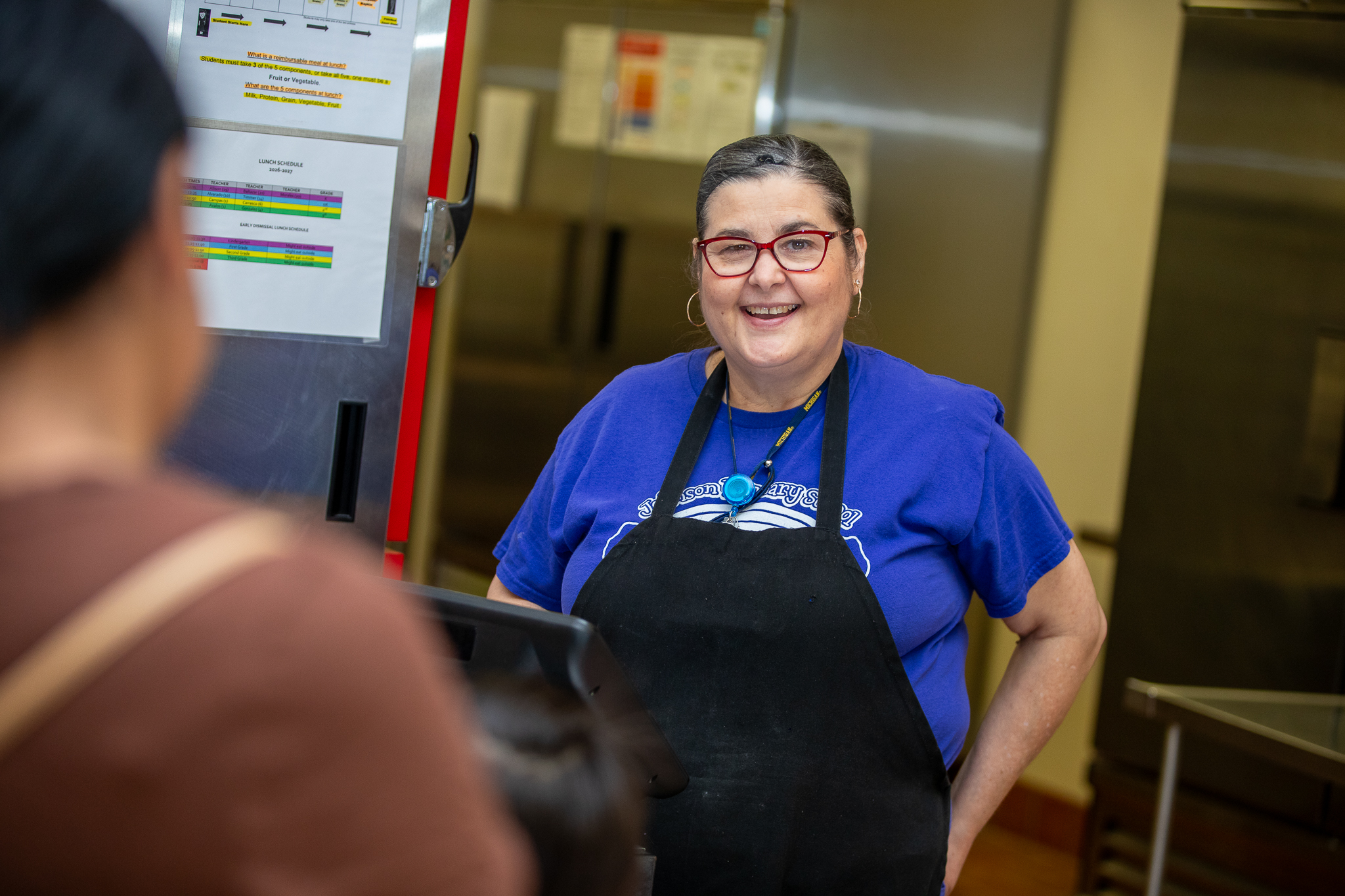 A cafeteria worker smiles as she serves a student breakfast