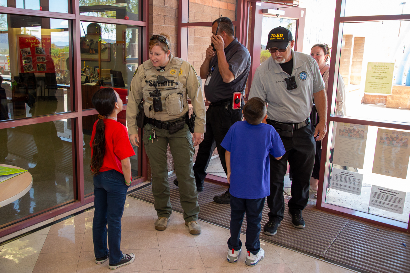 A Pima County Sheriff deputy and TUSD School safety officer talk with two students.